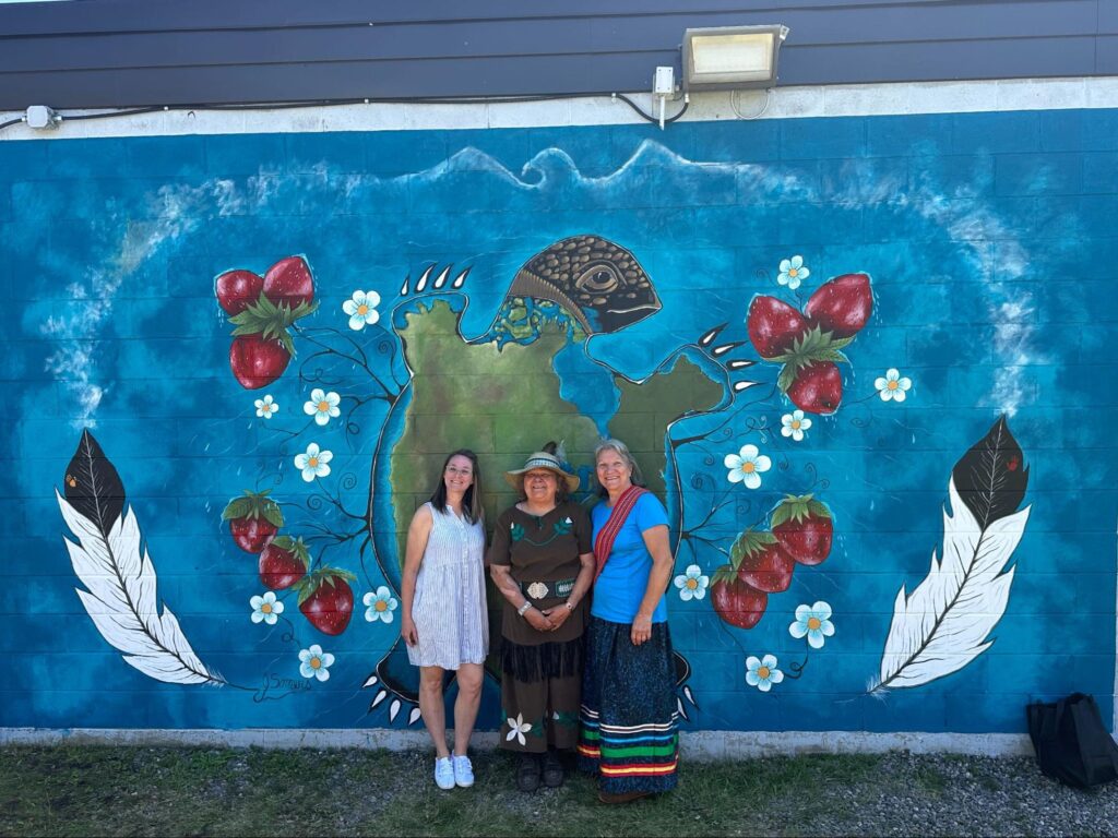 An artist working on an outdoor wall during sunny weather, contrasting with indoor studio planning for winter months, illustrating the seasonal nature of public art projects.